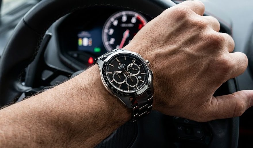 Relógio Rado Close-up de um relógio Rado HyperChrome Chronograph no pulso de um homem segurando o volante de couro de um carro esportivo luxuoso.