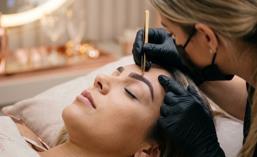 Designer de sobrancelhas realizando o método exclusivo do Curso Sobrancelhas Perfeitas em uma cliente, garantindo um design de sobrancelhas impecável.