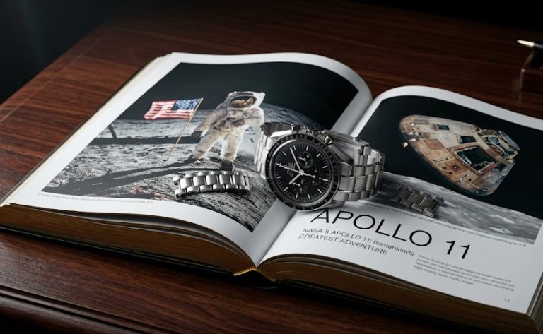 Relógio Omega Speedmaster Professional apoiado sobre um luxuoso livro de capa dura sobre as missões Apollo da NASA.