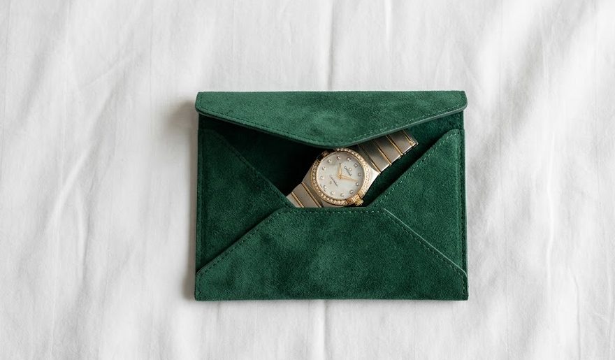 Relógio Omega Constellation refinado sendo guardado dentro de um elegante estojo individual tipo envelope (pouch) feito de camurça verde.