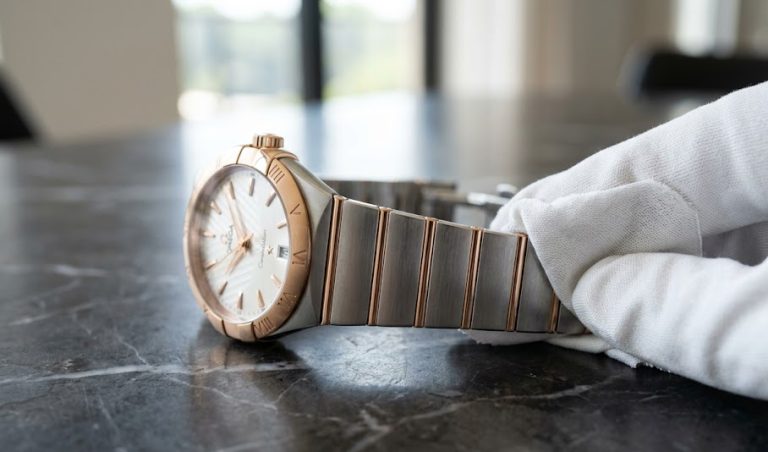 Flanela premium de algodão limpando cuidadosamente a pulseira de ouro e aço de um relógio estilo Omega Constellation.